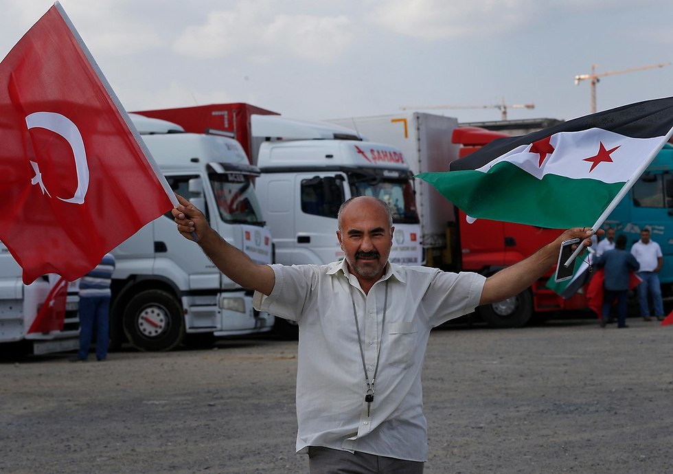 A man waves Syrian an Turkish flags as trucks carrying humanitarian aid leaves Turkey