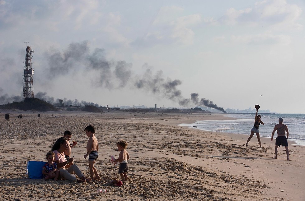 ישראלים בחוף זיקים ברקע עשן שריפת צמיגים ברצועת עזה (צילום: AP)