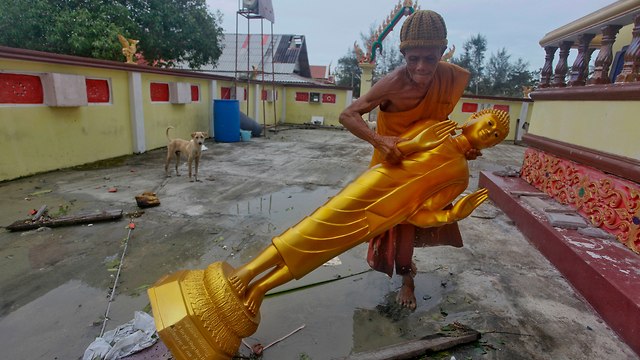 נזיר תאילנדי מפנה פסל של בודהה בנאקון סי טמרט, עם חלוף הסופה 