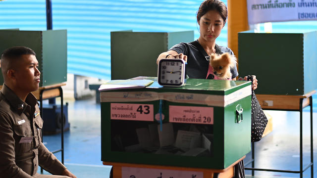 תאילנדית משלשלת את פתק ההצבעה בבנגקוק, לצד שומר שמאבטח את הקלפי (צילום: AFP)