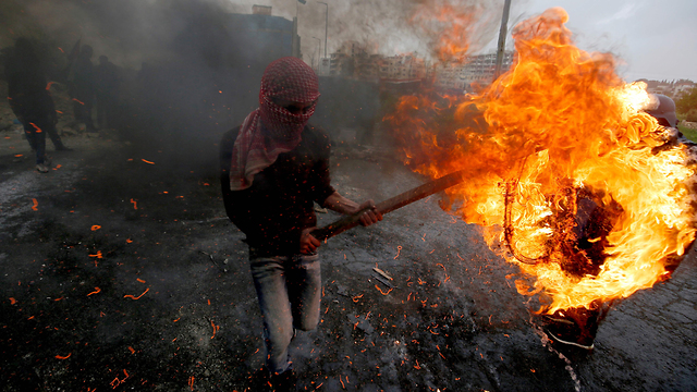 פלסטיני מבעיר צמיג בעימותים בגדר הגבול לציון צעדת השיבה ויום האדמה (צילום: AFP)