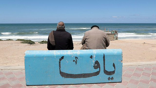 הדייג מחמוד אל-עאסי יושב על ספסל בטון בחוף בעזה ועליו הכיתוב 