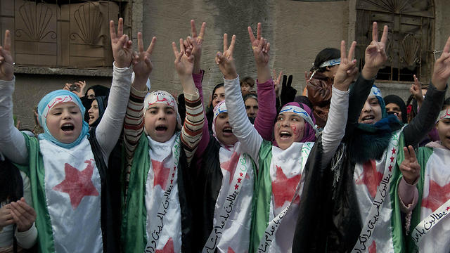 Anti-Syrian regime protesters flash the victory sign as they wear Syrian revolution flags during a demonstration in the Baba Amr area, in Homs province, Syria
