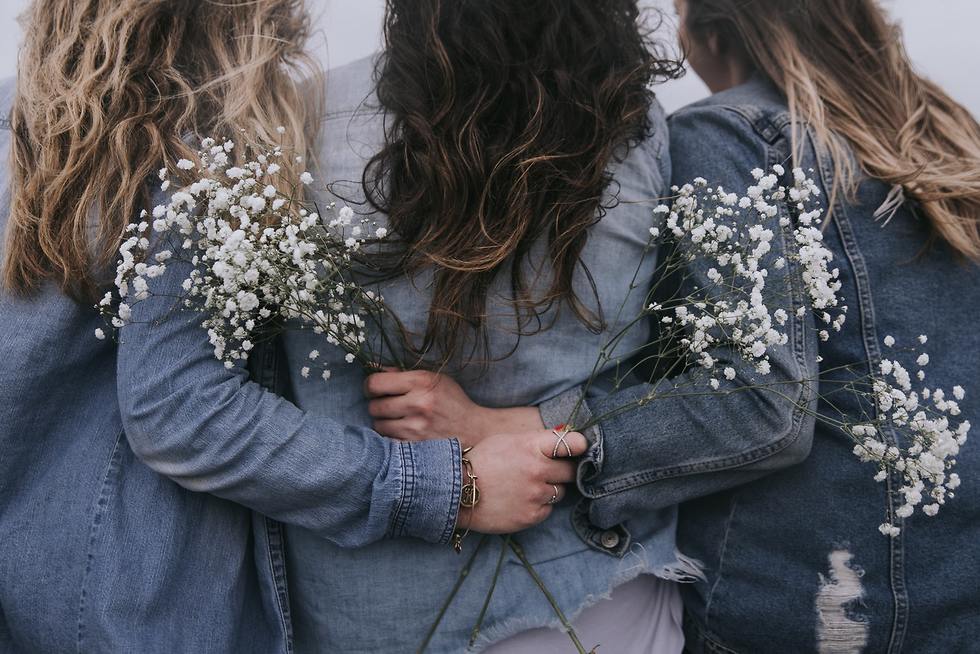 3 צעירות מחובקות עם פרחים מצולמות מאחור ()