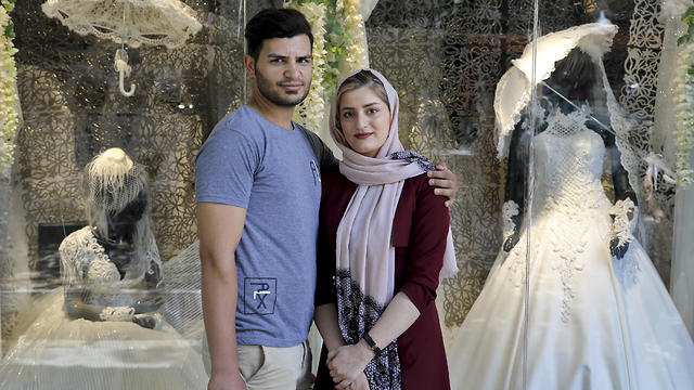 Newly married Iranian couple Mohammad Davoodi, 28, and his wife Mahsa Asadzadeh, 20, pose for a photo in front of a wedding dress shop in downtown Tehran, July 3, 2019 