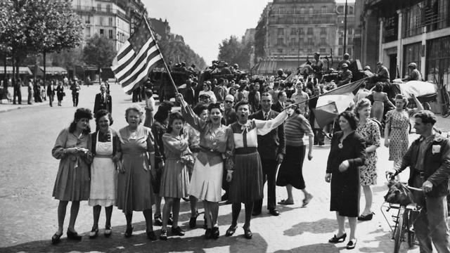French civilians with hastily made American and French flags greet U.S. and Free French troops entering Paris, France, after Allied liberation of the French capital from Nazi occupation in 