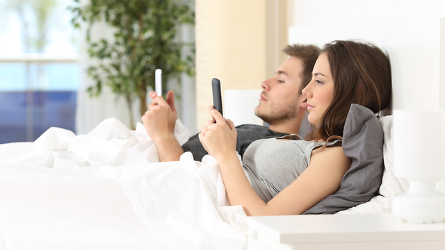 זוג שוכב במיטה ומתעסק בטלפון (צילום: shutterstock)