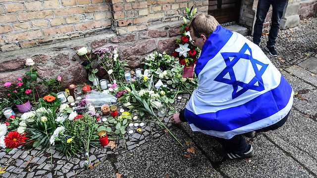 A man wrapped in an Israeli flag lays flowers at the site of the Halle synagogue shooting (Photo: EPA)