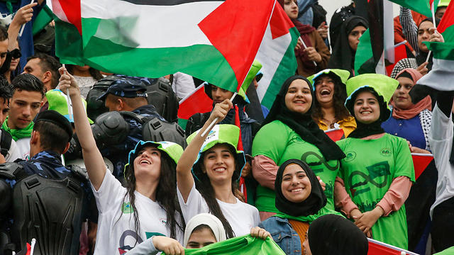 Women football fans wave Palestinian flags as they attend the World Cup 2022 qualifier match between Palestine and Saudi Arabia in the West Bank, Oct. 15, 2019  