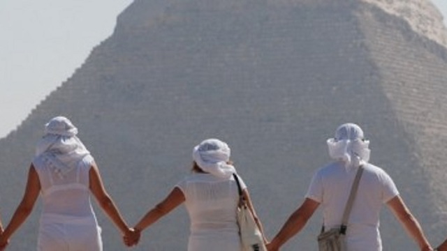 קבוצת אנשים לבושים לבן נותנים ידיים בגבם למצלמה אל מול הפירמידות ()