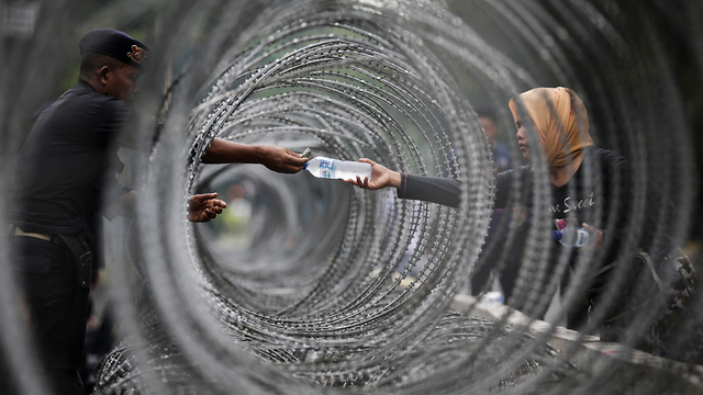 A policeman buying a water bottle from a woman through a barbed wire fence while he secures the Constitutional Court in Jakarta, Indonesia, July (Photo: EPA)