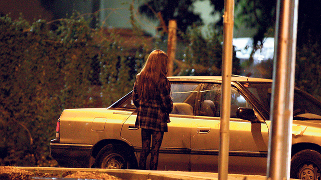 אישה בזנות עומדת עם הגב למצלמה ליד מכונית דוממת (צילום: גיל נחושתן)