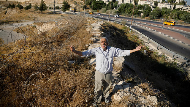 Palestinian man Ali Farun, 74, gestures by a road in al-Eizariya town with the Jewish settlement of Maale Adumim in the backgroundBank settlements