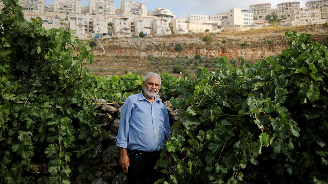 Palestinian man Mohammad Awad, 64, poses for a photo at his farm in the village of Wadi Fukin with the Jewish settlement of Beitar Illit in the background