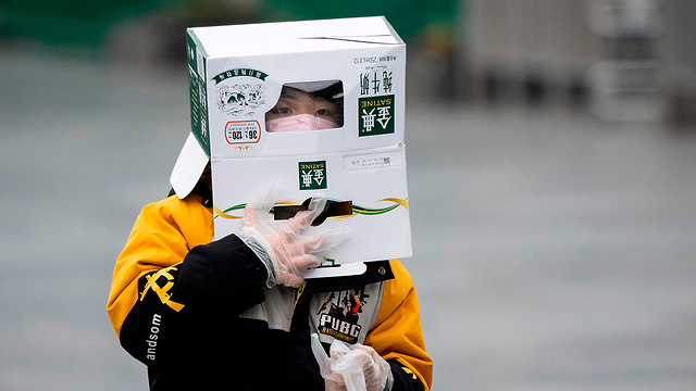 Житель Шанхая прикрывается картонной коробкой от коронавируса. Фото: AFP