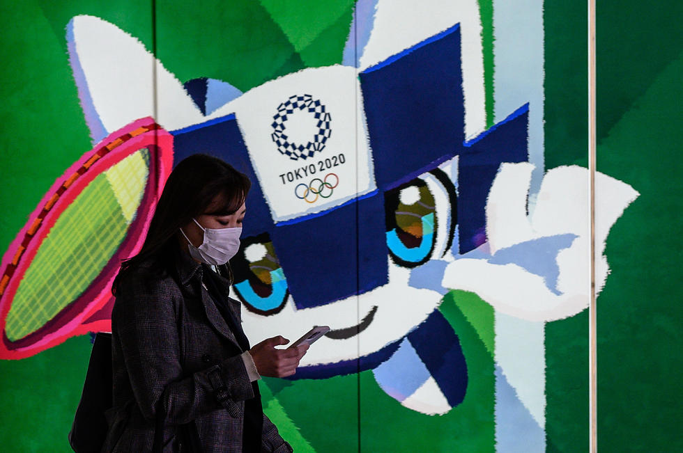 אזרחית יפנית ליד תמונת הקמע של המשחקים (צילום: AFP)