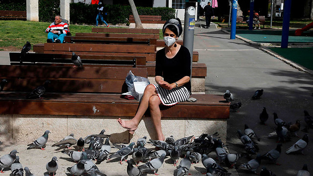 אישה עם מסכה יושבת על ספסל ב ירושלים (צילום: AFP)