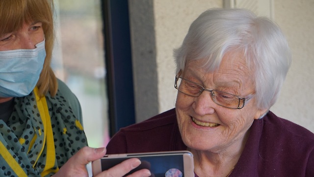 אישה מציגה טלפון נייד לקשישה  ()