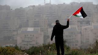 A man waves a Palestinian flag in front of an Israeli settlement in the West Bank 
