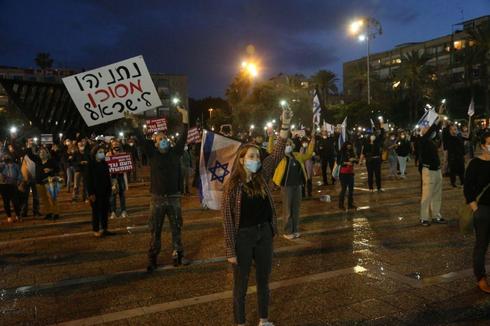 Des Israéliens masqués assistent à une manifestation à Tel Aviv contre l'accord de coalition. La bannière indique: Netanyahu est dangereux pour Israël (Photo: Moti Kimchi) מחאת הדגלים השחורים בכיכר רבין