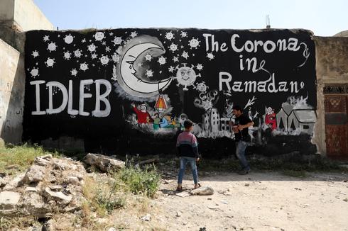 El pueblo sirio se encuentra cerca de un graffiti pintado debido a la pandemia en curso de la enfermedad de Covid-19, en Idlib, Siria