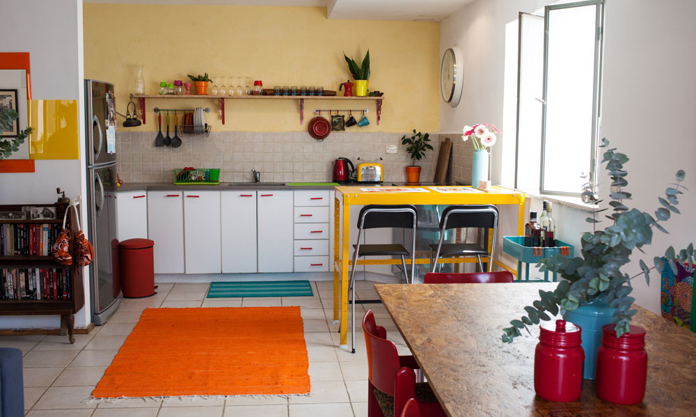 ארונות הפורמייקה הלבנה במטבח הושארו כפי שהם, אך קיר המטבח נצבע בצהוב ולדלתות הורכבו ידיות חדשות, קווים אדומים שמשתלבים בפסיפס הצבעוני סביב (צילום: יוראי לברמן)