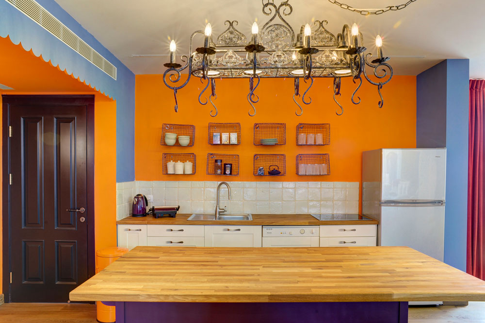 המטבח נצבע בכתום ו''מוסגר'' בכחול (משמאל דלת הכניסה לדירה). למטה ארונות לבנים פשוטים מ''איקאה'', שעליהם הוברגו ידיות שהוכנו ממזלגות. ה''אי'' נצבע סגול (צילום: Hadrien Daudet)