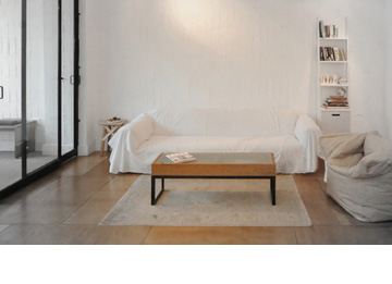 הסלון. ספה מכוסה בבד לבן, כורסת קרטון ושני רהיטים שעיצב טרוים: שולחן קפה וספרייה לבנה (צילום: עומרי אמסלם)