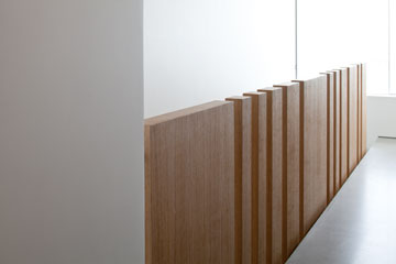 אלמנט העץ שמפריד בין המדרגות לסלון אינו מסתיים בתקרה, אלא משמש כמעקה בקומה העליונה (צילום: עמית גרון)