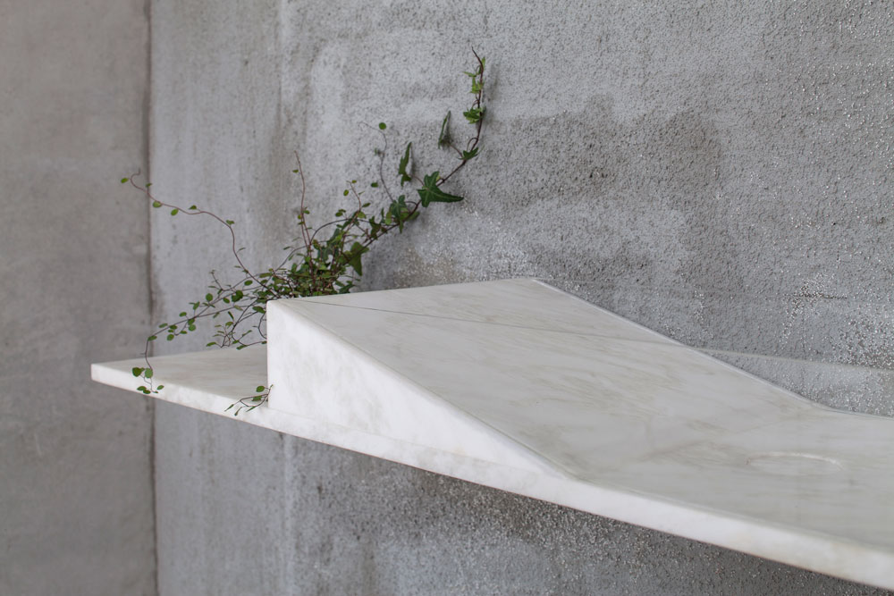 חתיכה אחת של אבן לבנה משמשת ככיור וכמדף, שתלוי על הקיר. דפנות הכיור עשויים זכוכית שקופה (צילום: עמית גרון)