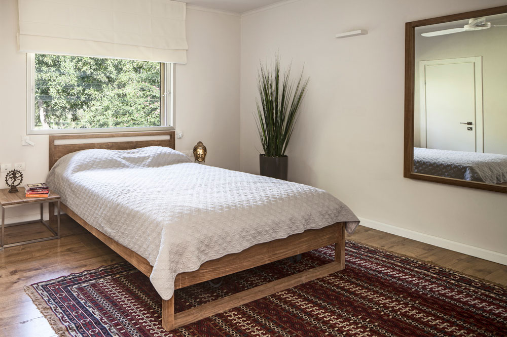 בחדר ההורים שבקומה העליונה עומדת מיטת עץ מתחת לחלון, ולרגליה שטיח קילים בצבעי אדמה (צילום: עמית גרון)