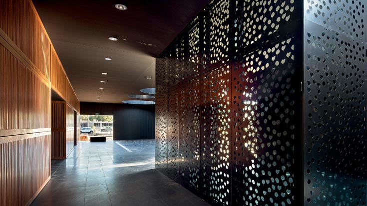 לוחות מתכת מנוקבים בצלליות של פרחי פרג יוצרים מסך של אורות סביב חדר תפילה בצורת ביתן מזוגג