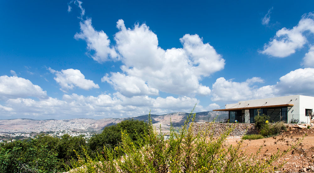 בני הזוג קורלנד חיכו זמן רב למגרש בישוב הקהילתי מכמנים, וזאת משום שביקשו מגרש מסוים מאוד: זה שבקצה ההרחבה, מול הנוף הפתוח של בקעת בית כרם וכרמיאל SaaB אדריכלים לוסיאנו סנטנדראו בית מכמנים
